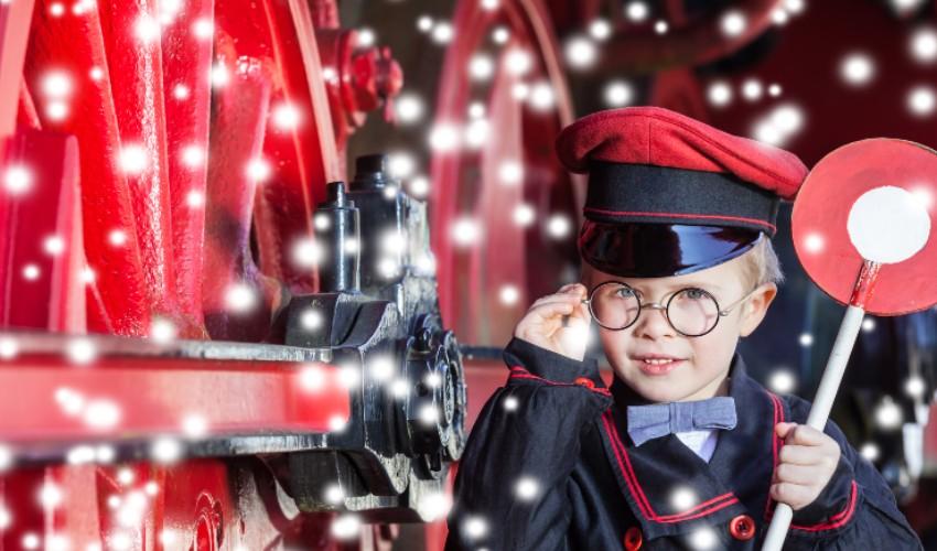 A boy in a suit and hat standing next to a red train.