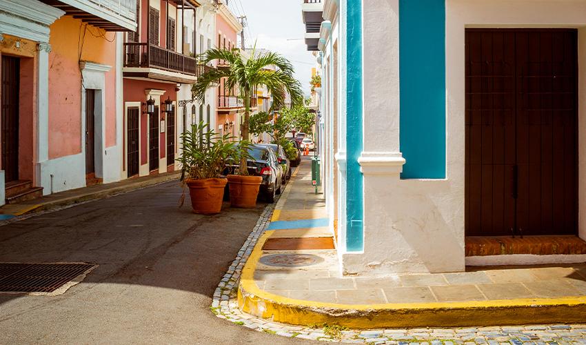 A narrow street lined with colorful buildings and parked cars.