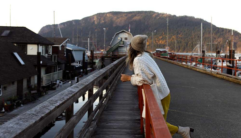 A woman is standing on a wooden pier looking at boats.