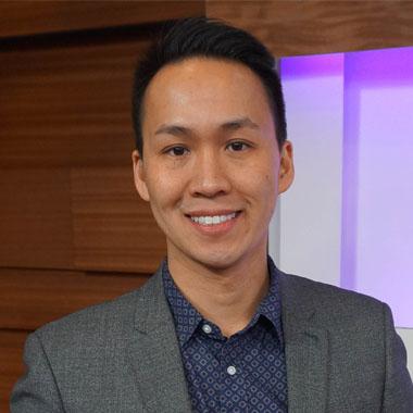 A man in a gray suit smiling in front of a television.